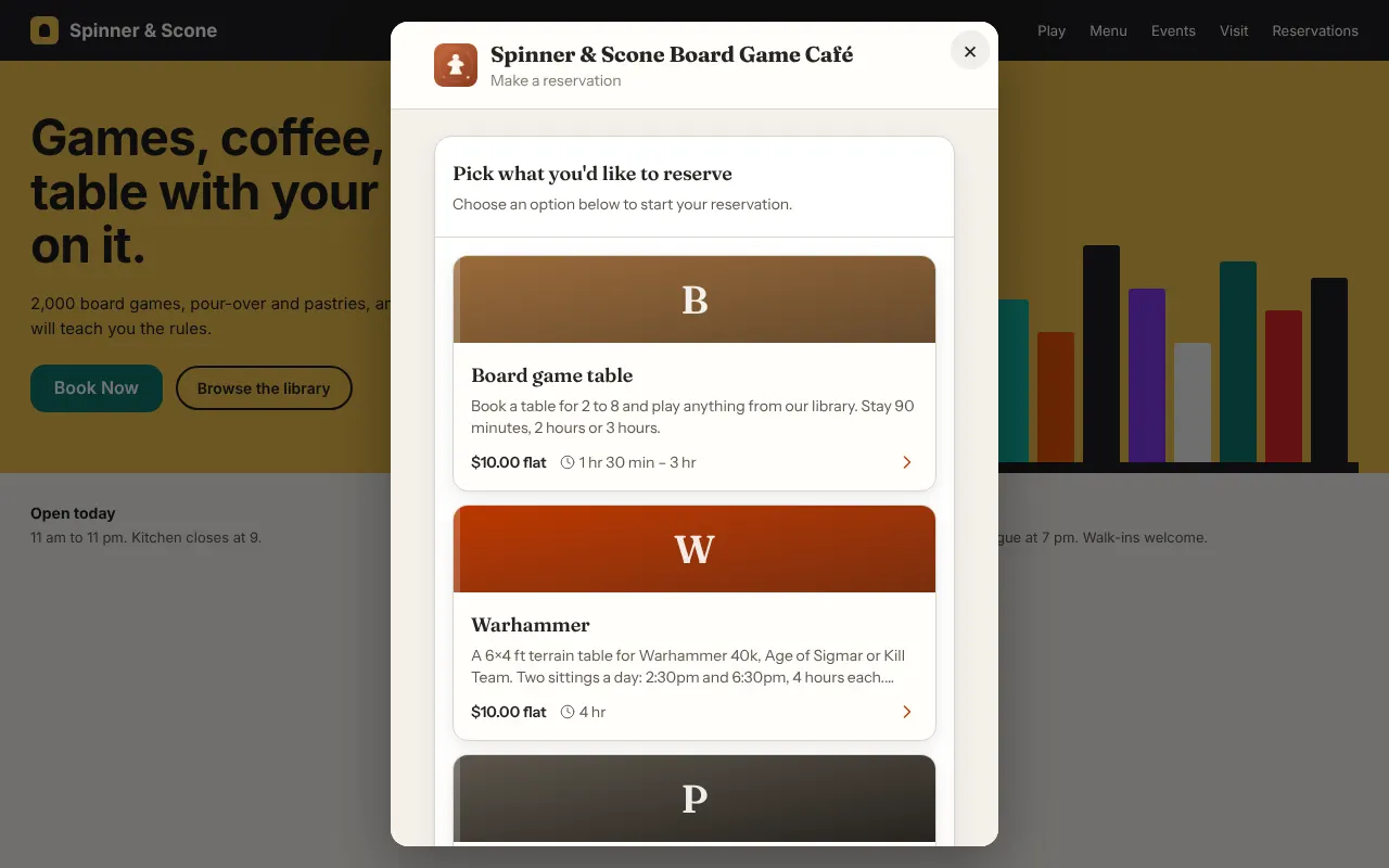 A café website dimmed behind a booking window. The window shows the Spinner & Scone Board Game Café header and the first reservation types: Board game table and Warhammer, with a third below.